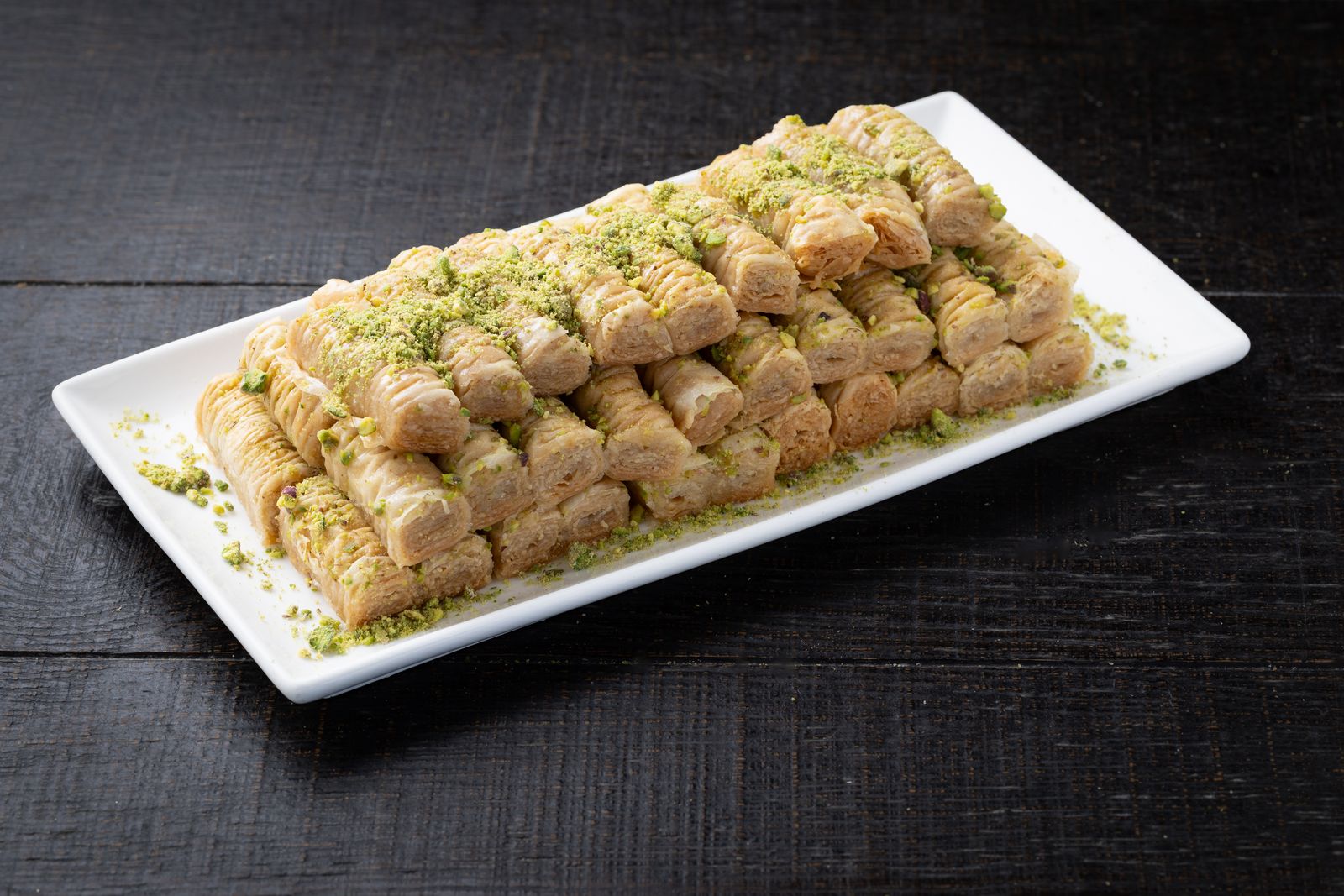 A platter of baklava fingers topped with crushed pistachio