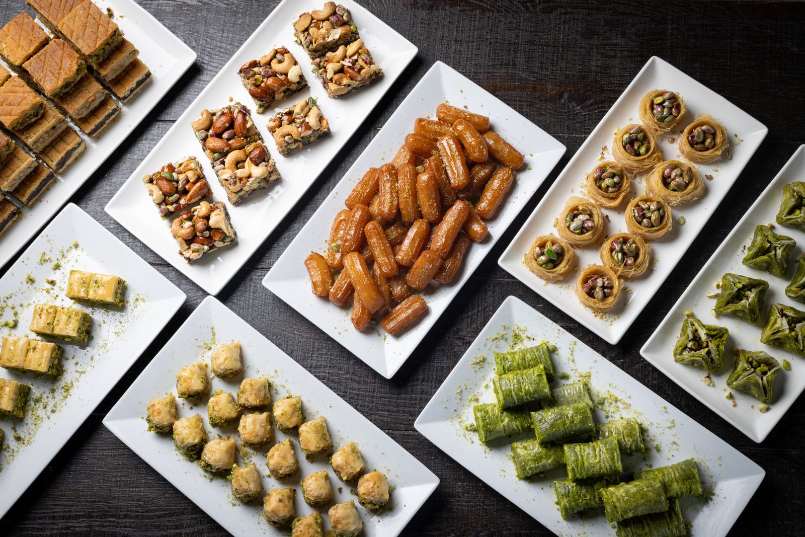 Platters of assorted baklava, ma'amoul and pistachio sweets on a dark wooden table